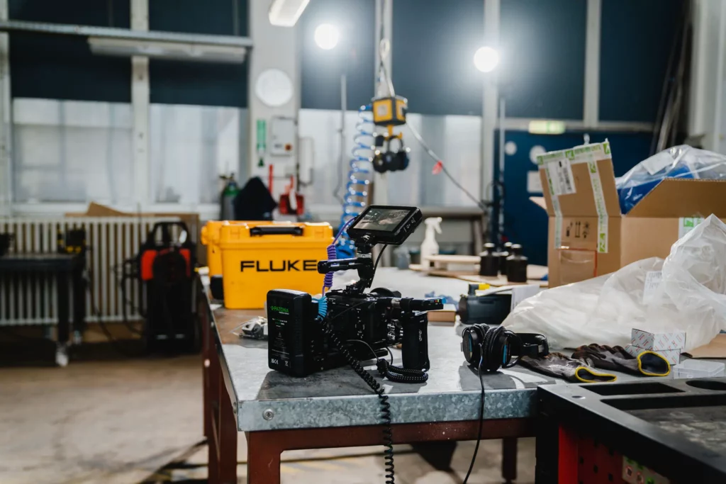 Kameraausrüstung mit Monitor und Kopfhörer auf einem Werktisch bei einem Imagefilm-Dreh in einer Industriehalle
