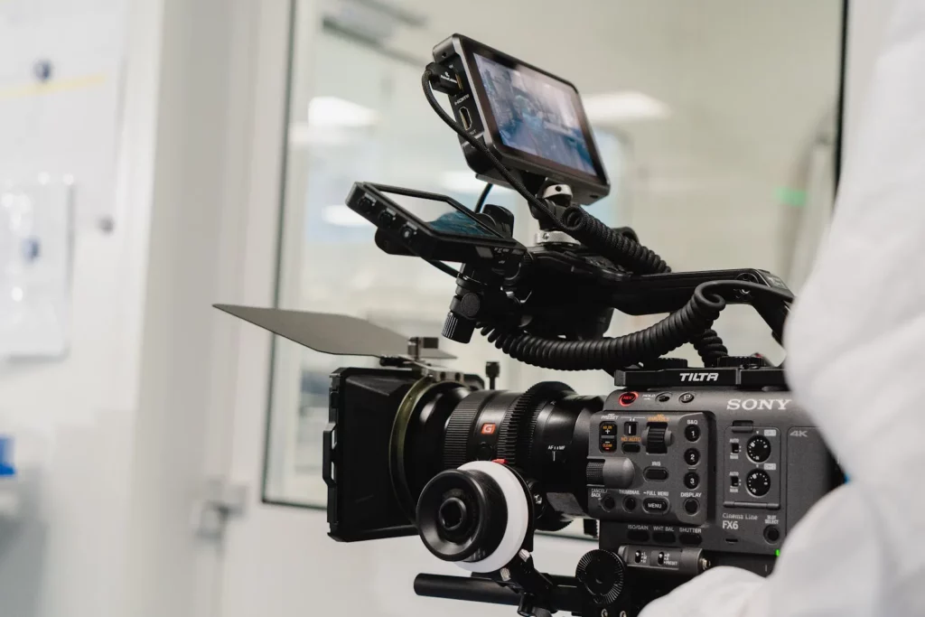Professionelle Filmkamera mit Kontrollmonitor und Schärferad in einem hellen Raum, gehalten von einer Person in weißer Schutzkleidung